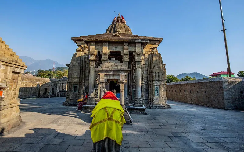 Devotee walking toward the ancient stone Nagara architecture of historic Baijnath Temple
