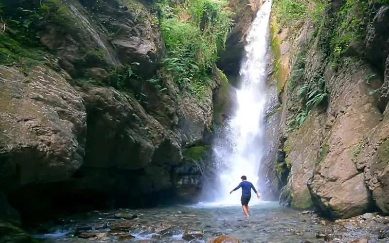 Hiker standing near the spray of secluded Bangoru Waterfall cascading down rocky gorge near Bir