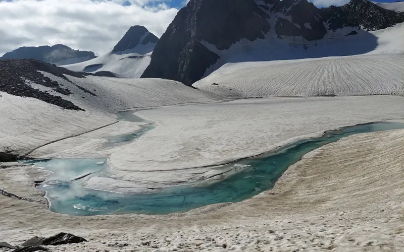 High-altitude glacial lake and melting snowfields surrounded by rugged rocky mountain ridges on Bara Bhangal trek