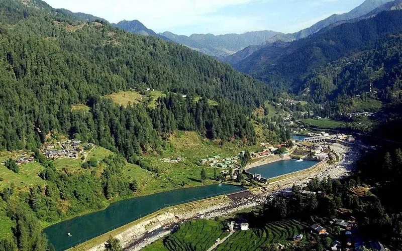 Aerial view of Barot reservoir lake nestled inside a lush green valley framed by forested hills