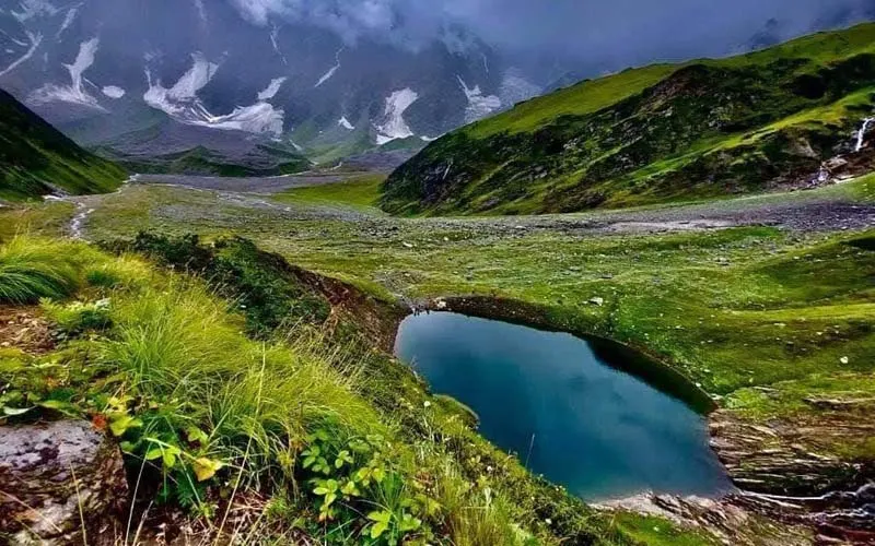 Emerald waters of high-altitude Beas Kund glacial lake surrounded by green alpine ridges near Manali