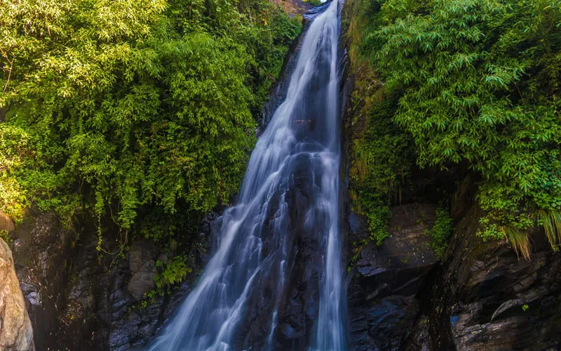 Bhagsu Waterfall cascading over rocky green cliffs in McLeod Ganj
