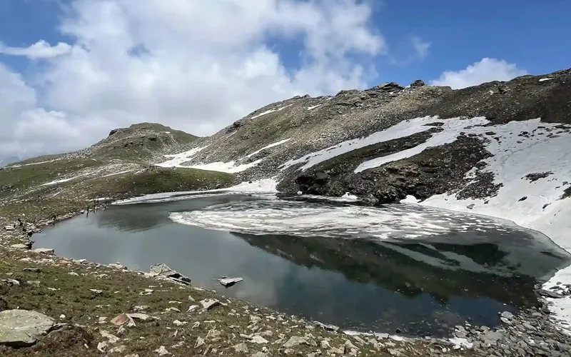 High-altitude glacial waters of Bhrigu Lake surrounded by rugged scree slopes and snow patches