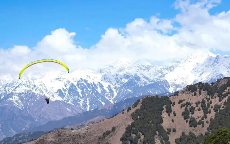 Tandem paraglider flying high above mountain slopes with snow-capped Himalayan peaks in Billing