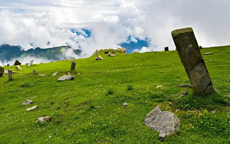Ancient upright stone monoliths on lush green high-altitude alpine meadows on Chandrakhani Pass trek