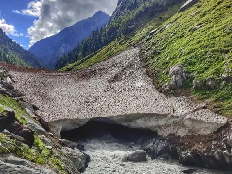Rushing glacial stream emerging from beneath a giant natural snow bridge in Bara Bhangal
