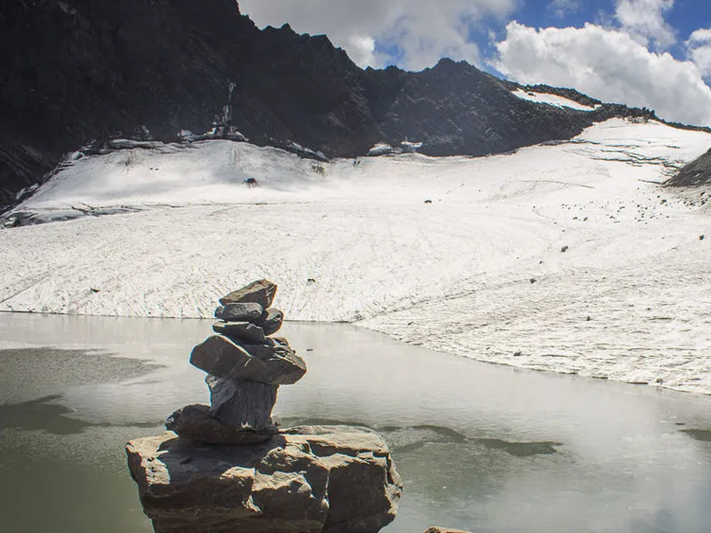 Stone cairn balancing on a rock overlooking a frozen glacial lake and massive snowfields