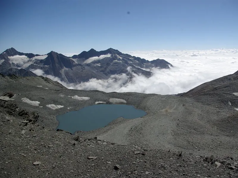 High-altitude alpine glacial tarn surrounded by scree and sea of clouds in Bara Bhangal
