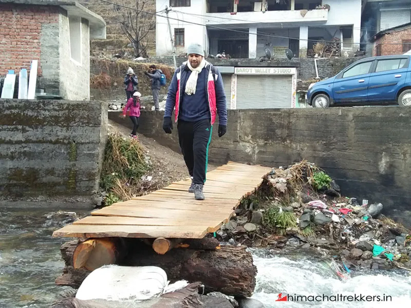 Trekker crossing a wooden plank bridge over a mountain stream in Barot village