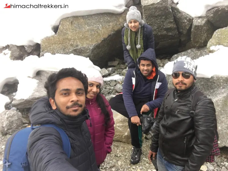Group selfie of trekkers resting near rocky boulders during winter trek in Barot