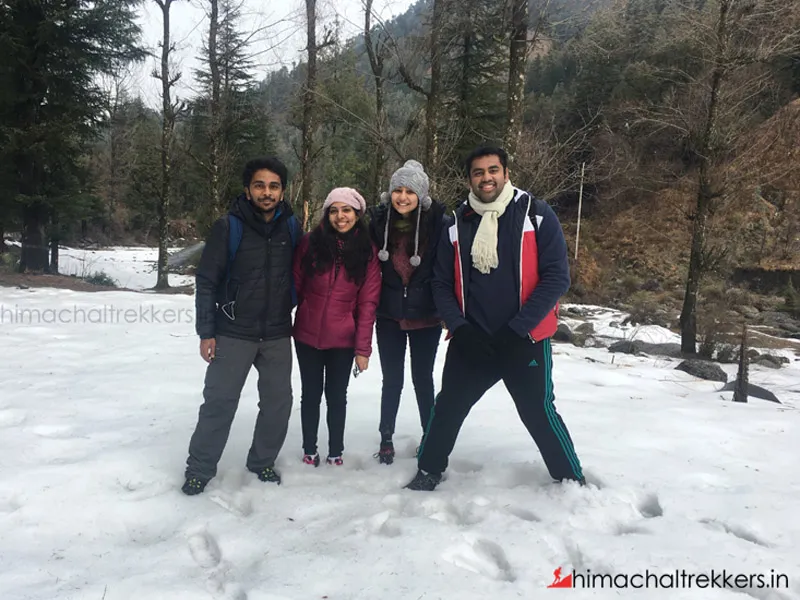 Trekking team standing on thick winter snow surrounded by tall pine trees in Barot Valley