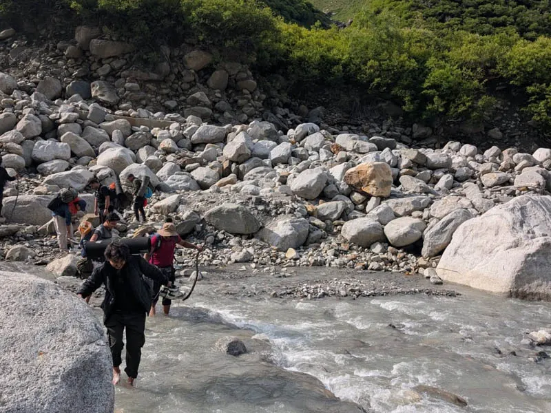 Trekkers wading through a rocky mountain stream during Beas Kund trek