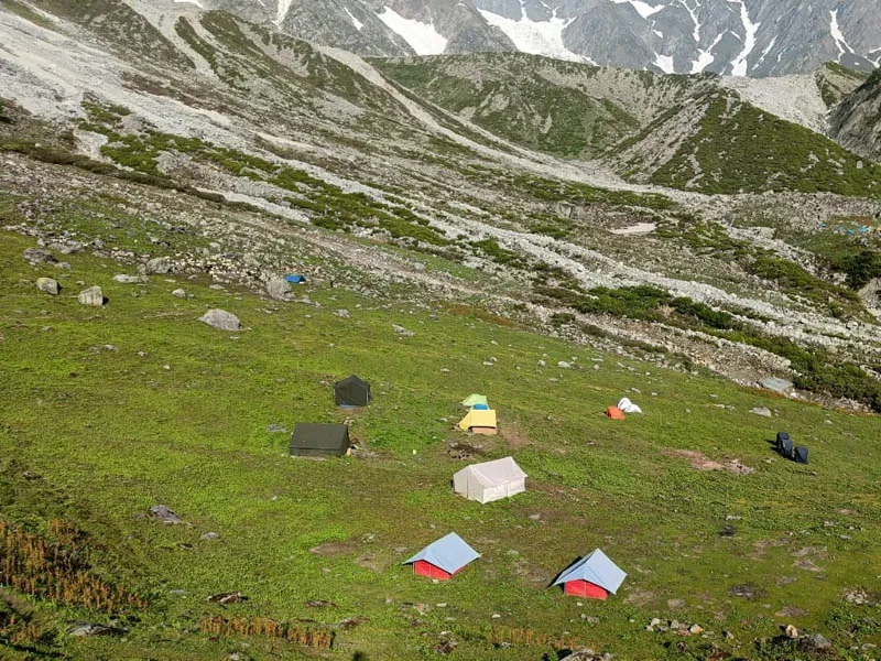 Colorful alpine camping tents pitched on green meadows beneath rocky mountain ridges