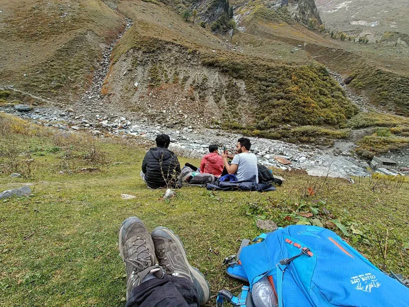 Hikers relaxing near a campsite with mountain stream views on the Beas Kund trail