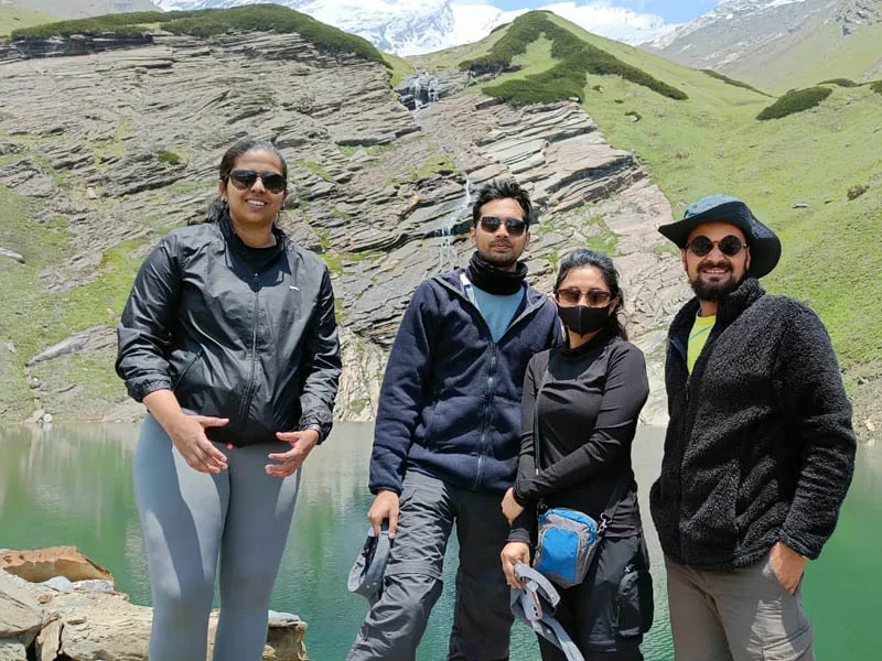 Four trekkers posing happily on the shores of sacred Beas Kund alpine lake