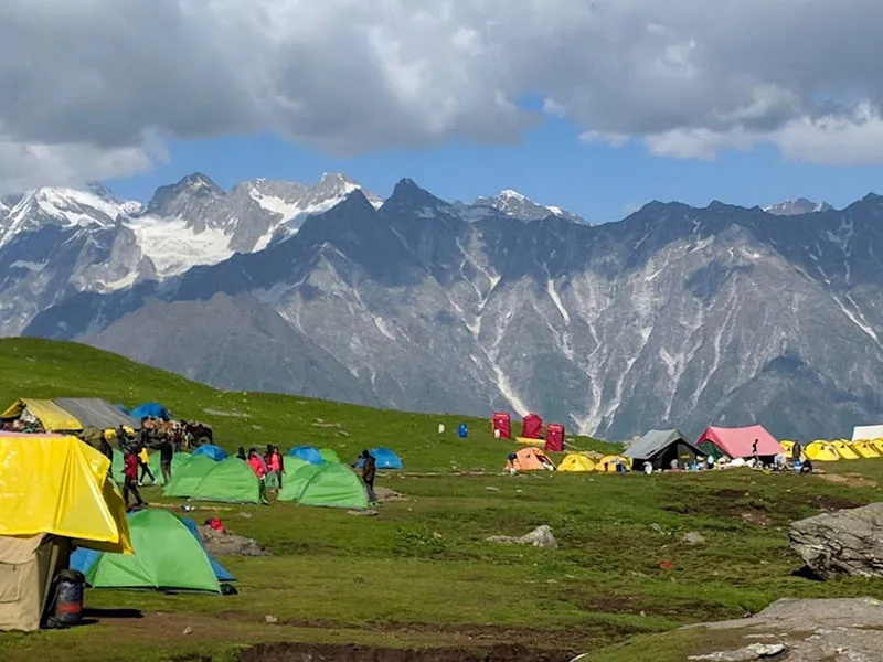 Colorful camping tents pitched in a high alpine meadow with snow peak backdrop
