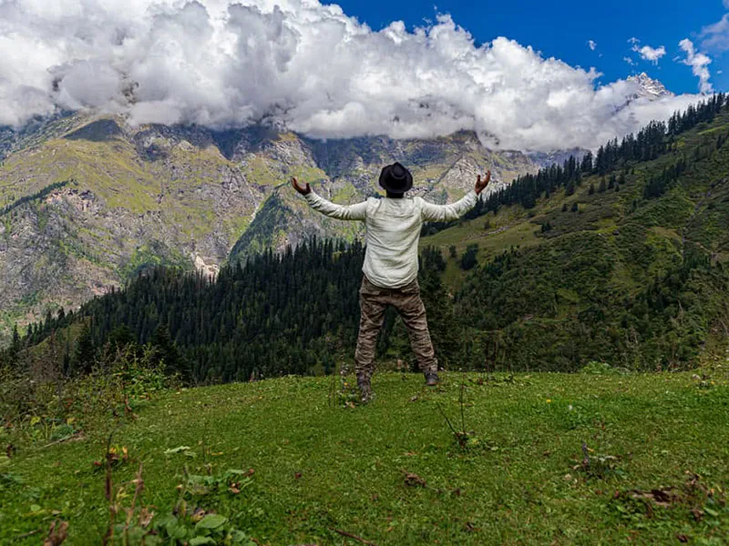Trekker standing with open arms celebrating on a high mountain ridge facing cloudy peaks
