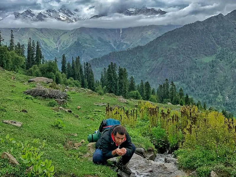 Hiker drinking fresh natural spring water from a mountain stream in lush green valley