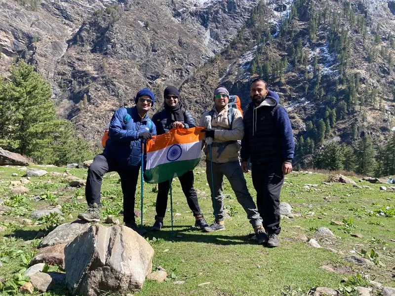 Trekking group proudly holding the Indian national flag on a sunny mountain clearing