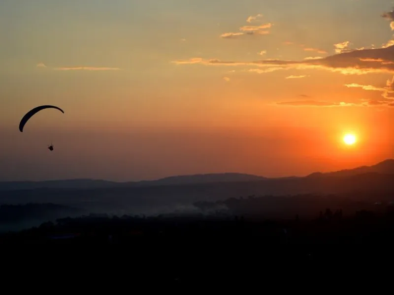 Silhouette of a paraglider flying against a vibrant golden-orange sunset sky over Bir Billing