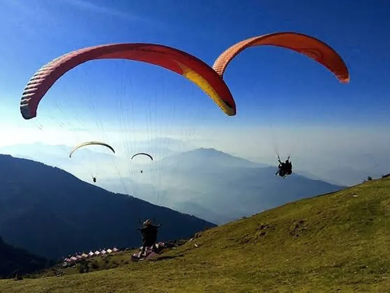 Bright red and yellow paraglider taking off from the grassy mountain launch site at Billing