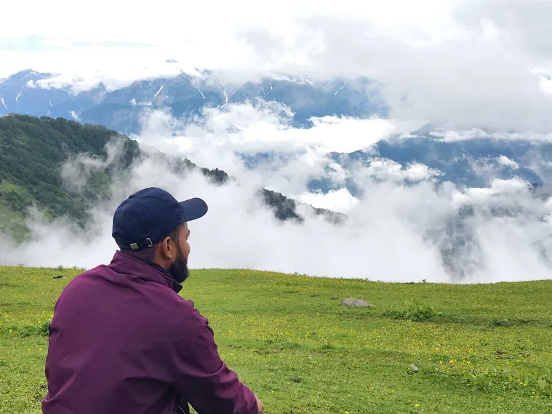 Trekker admiring rolling clouds and green mountain meadows on Chandrakhani Pass trek
