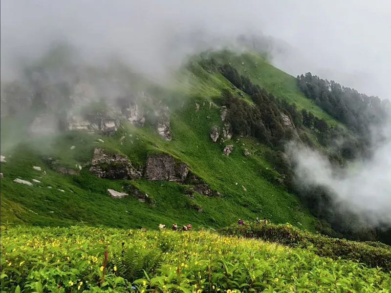 Lush green mountain slopes wrapped in low-hanging monsoon clouds