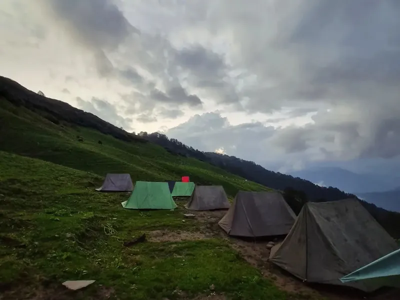 High-altitude alpine tents pitched on green ridge under dramatic cloudy skies