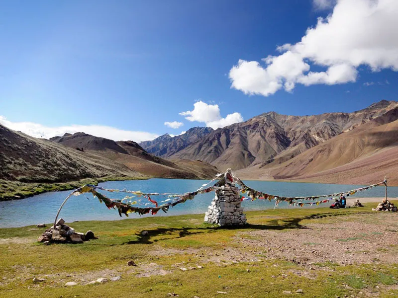 Prayer flags strung along the shore of blue Chandratal Lake with barren mountain peaks in the background