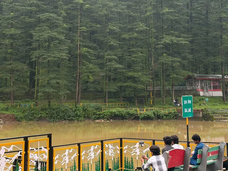 Visitors sitting along the fenced railing of scenic Dal Lake surrounded by deodar woods in Dharamshala