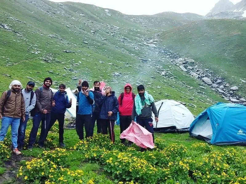 Trekking group standing near pitched alpine tents at a mist-covered campsite