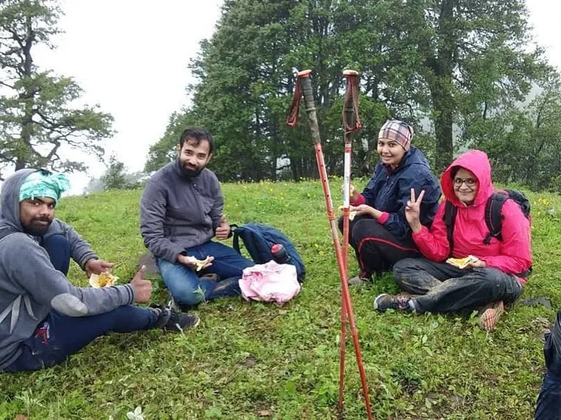 Hikers relaxing and having a meal on green meadows near trekking poles