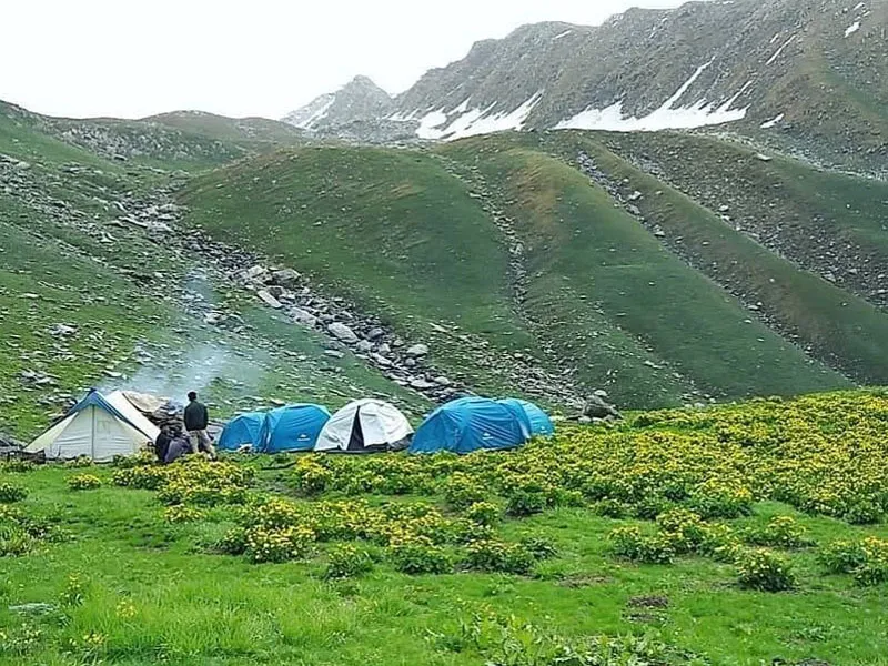 High-altitude campsite with colorful tents set against snow-streaked alpine mountain slopes