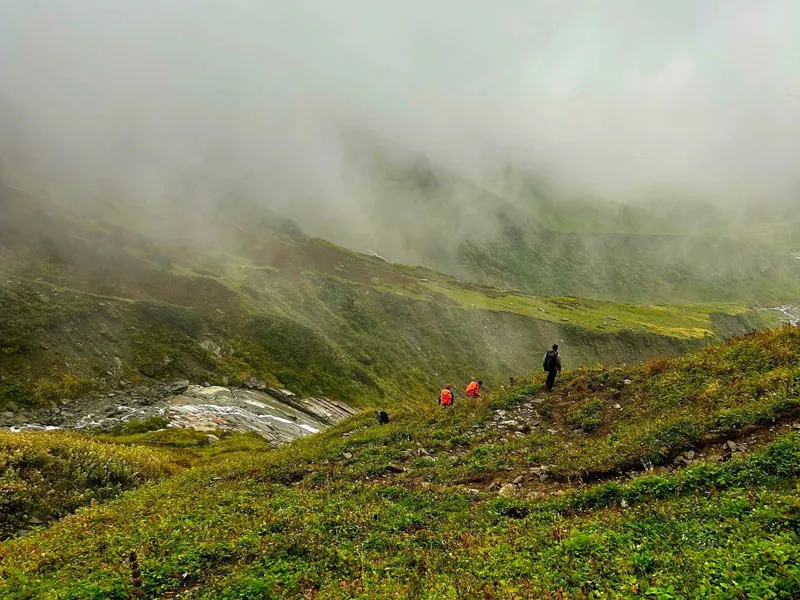 Trekkers ascending a misty green alpine ridge on the Friendship Peak trail