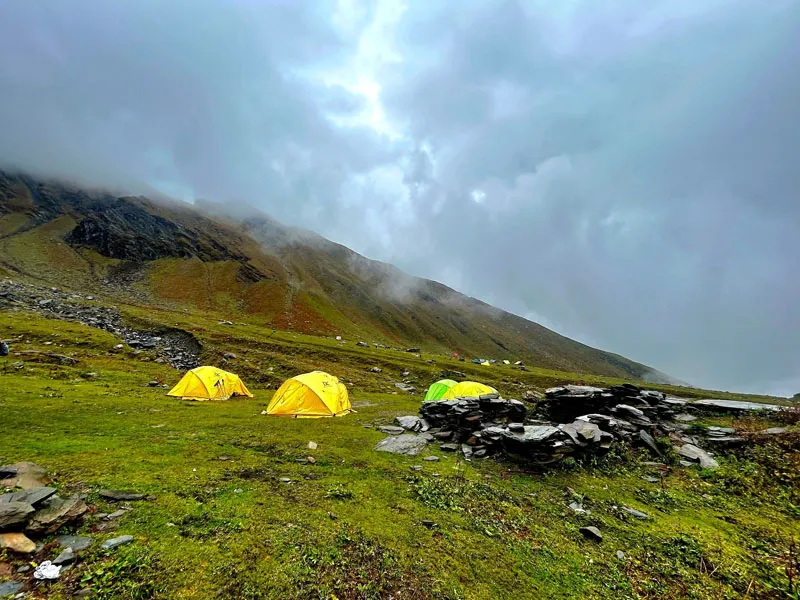 Bright yellow camping tents pitched on a grassy slope under dramatic monsoon clouds