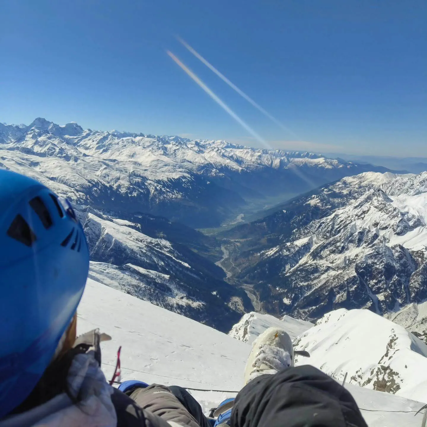 Climber wearing blue helmet looking down at expansive snow-capped Himalayan ranges from the summit ridge