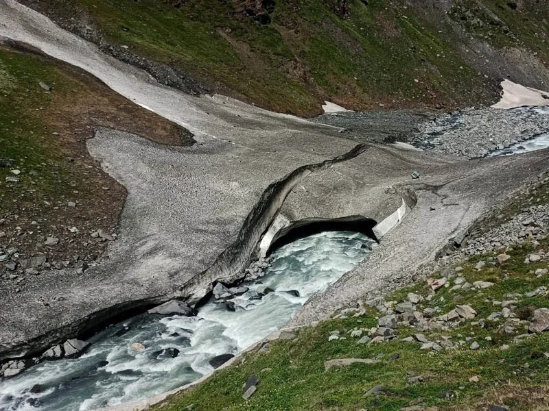 Glacial river flowing underneath a natural snow bridge in a rocky Himalayan valley