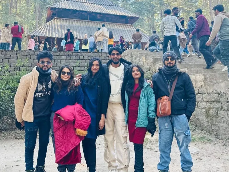 Group of friends posing outdoors in front of ancient stone wall and Hadimba Temple in Manali