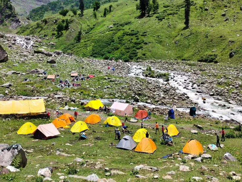 Chika campsite with colorful yellow and orange tents pitched along a rushing river on Hampta Pass trek