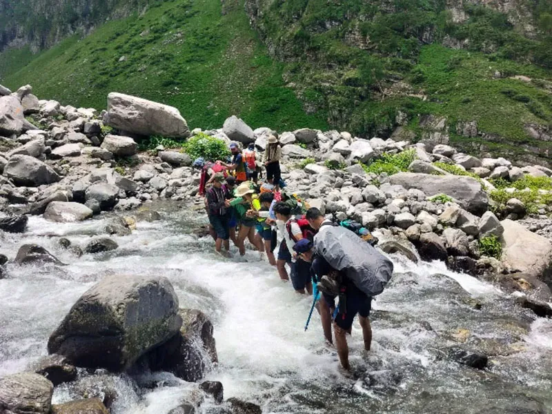 Trekkers forming a human chain to cross a freezing cold mountain river during Hampta Pass trek