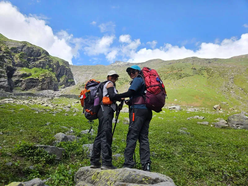 Two trekkers carrying large backpacks taking a rest in green alpine meadows on the Hampta trail
