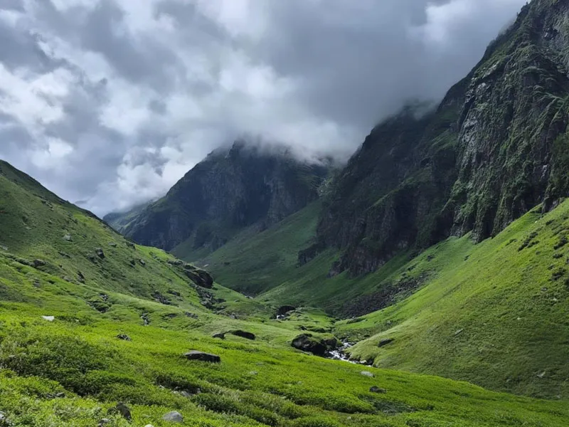 Dramatic view of steep green valley walls and hanging clouds in the Kullu region of Hampta Pass