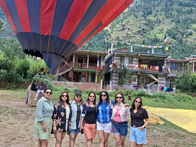 Group of women posing outdoors in front of a colorful tethered hot air balloon ride in Kullu Valley