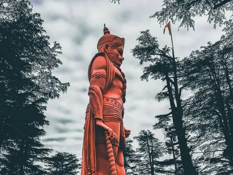 Colossal red statue of Lord Hanuman at Jakhoo Temple rising above pine tree canopy in Shimla