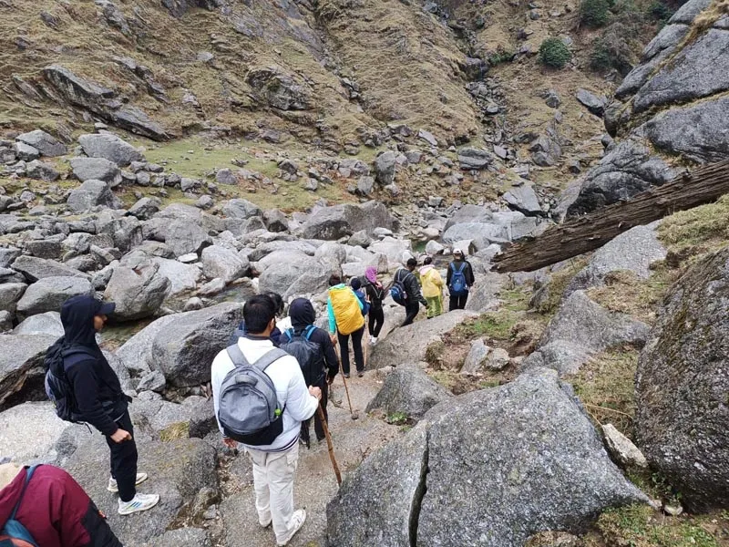 Hikers walking single file over giant river boulders on Kareri Lake trek