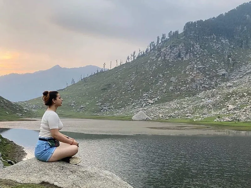 Solo girl sitting peacefully and meditating by the rocky shore of Kareri Lake