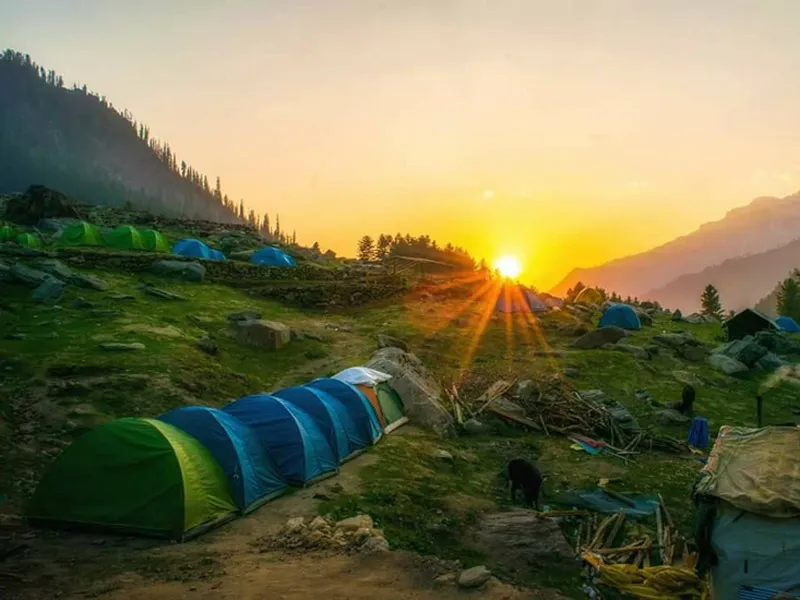 Tents pitched at an alpine campsite illuminated by a glowing sunrise in the mountain valley