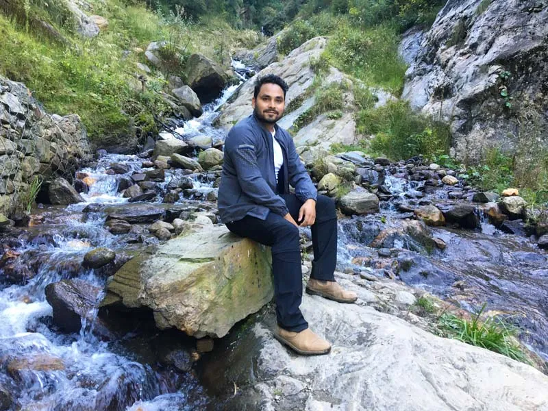 Hiker sitting on a rock by a rushing freshwater mountain stream on the Kheerganga trail