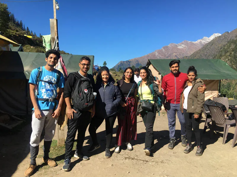 Trekking group standing together at Kheerganga campsite with mountain backdrop