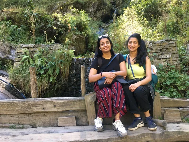 Two female hikers taking a rest on a wooden bench along the scenic Parvati Valley trek